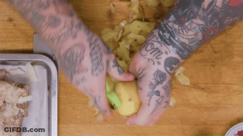 A Man With A Lot Of Tattoos On His Arms Is Peeling A Potato GIF