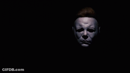 A Man With A Mask On His Face Holds His Hand Up In The Dark GIF