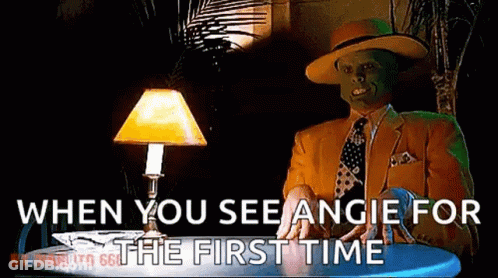 A Man With A Mask On His Face Is Sitting At A Table With A Lamp And Says When You See Angie For The First Time GIF