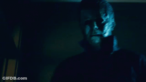 A Man With A Mask On His Face Is Standing In A Dark Room Looking At The Camera GIF