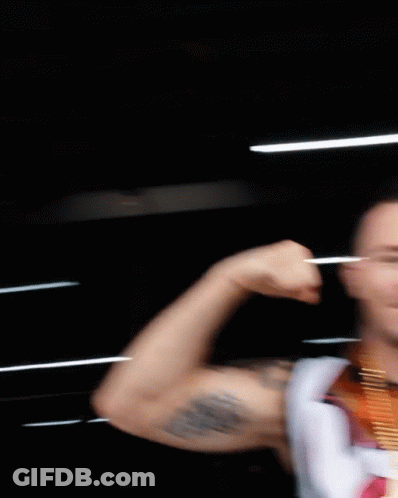 A Man With A Medal Around His Neck Flexes His Arm GIF