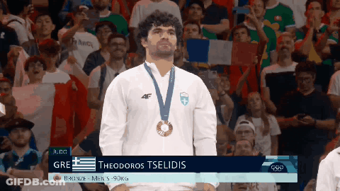 A Man With A Medal Around His Neck Is Standing In Front Of A Crowd GIF