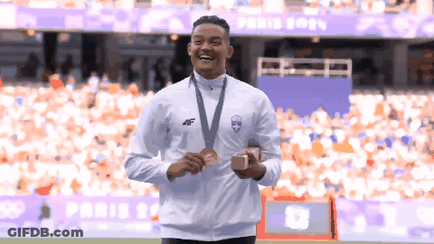 A Man With A Medal Around His Neck Stands In Front Of A Stadium That Says Paris 2021 GIF