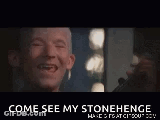 A Man With A Missing Tooth Is Laughing In Front Of A Mirror With The Words `` Come See My Stonehenge '' Below Him . GIF