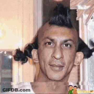 A Man With A Mohawk And Pigtails On His Head Is Standing In Front Of A Window . GIF