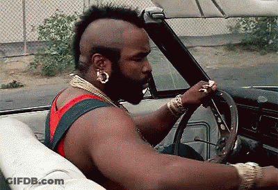 A Man With A Mohawk Is Driving A Car With His Hand On The Steering Wheel GIF