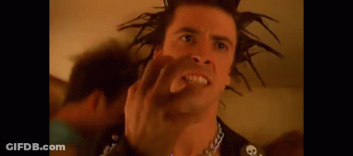 A Man With A Mohawk Is Making A Funny Face While Wearing A Chain Around His Neck . GIF