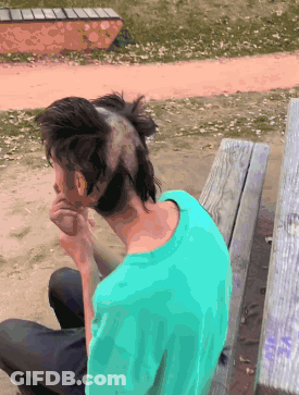 A Man With A Mohawk On His Head Sits On A Wooden Bench GIF