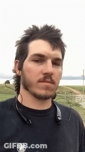 A Man With A Mullet And A Beard Is Wearing A Black Shirt GIF