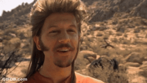 A Man With A Mullet And A Beard Smiles In The Desert GIF