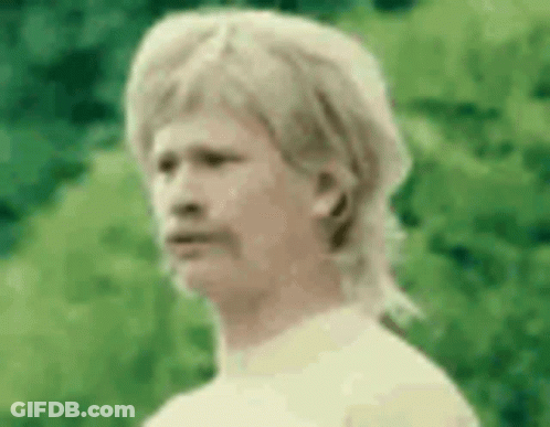 A Man With A Mullet And A Mustache Is Standing In Front Of A Green Background . GIF