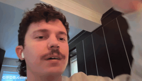 A Man With A Mullet And A Mustache Is Wearing Ear Buds GIF