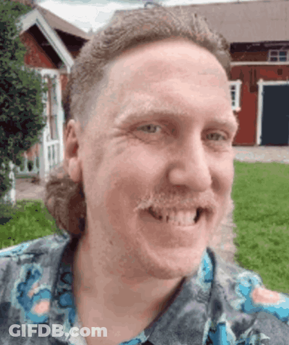A Man With A Mullet And A Mustache Smiles In Front Of A Red Barn GIF