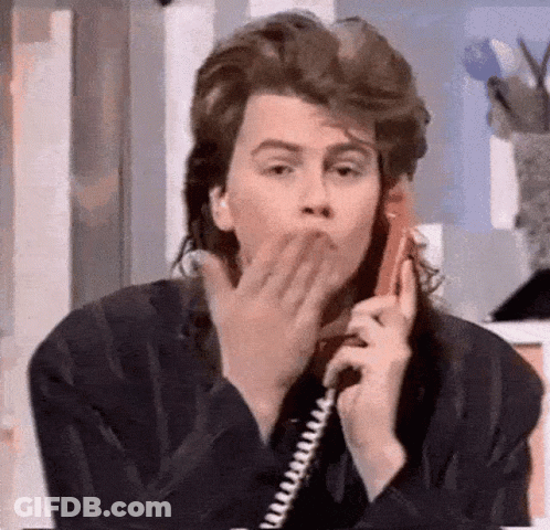 A Man With A Mullet Is Blowing A Kiss While Talking On A Phone . GIF