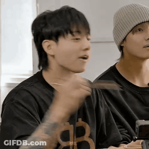 A Man With A Mullet Is Eating Food With Chopsticks While Sitting At A Table . GIF