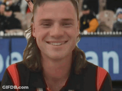 A Man With A Mullet Is Smiling In Front Of A Sign That Says Open GIF