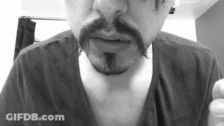 A Man With A Mustache And A Beard Is Wearing A Black Shirt In A Black And White Photo . GIF