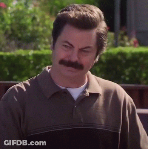 A Man With A Mustache And A Brown Shirt Looks At The Camera GIF
