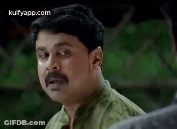 A Man With A Mustache And A Green Shirt Is Making A Funny Face . GIF