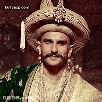 A Man With A Mustache And A Hat Is Wearing A Traditional Indian Outfit . GIF