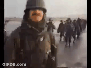 A Man With A Mustache And A Helmet Is Standing In Front Of A Group Of People . GIF