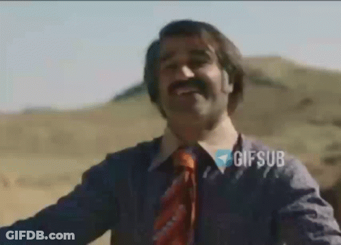 A Man With A Mustache And A Tie Is Smiling While Standing In The Desert . GIF
