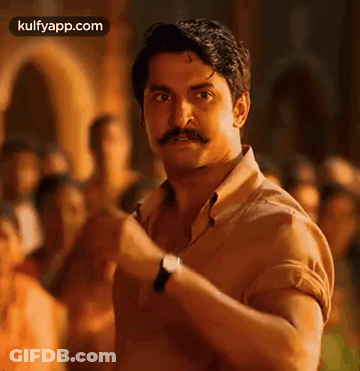 A Man With A Mustache And A Watch Is Standing In Front Of A Crowd Of People . GIF