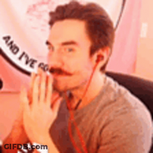 A Man With A Mustache And Ear Buds Is Sitting In Front Of A Pink Sign . GIF