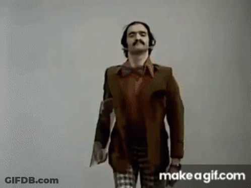 A Man With A Mustache And Headphones Is Standing Next To A Woman In A Plaid Shirt . GIF