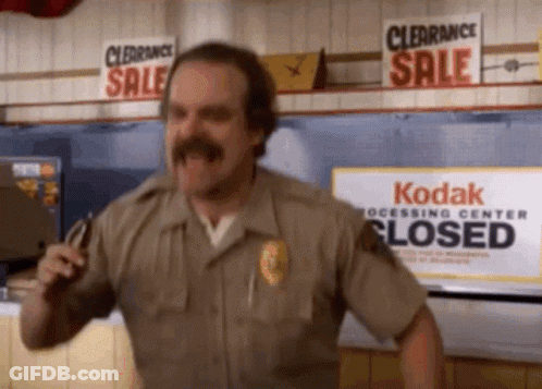 A Man With A Mustache Is Dancing In Front Of A Kodak Processing Center Closed Sign . GIF