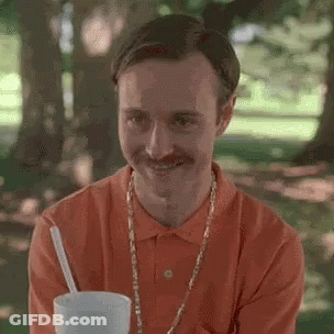 A Man With A Mustache Is Drinking A Milkshake In A Park . GIF