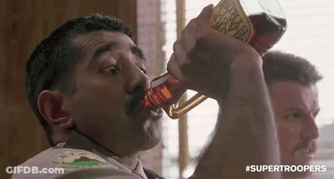 A Man With A Mustache Is Drinking From A Bottle With A Label That Says ' Supertroopers ' On It . GIF