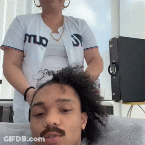 A Man With A Mustache Is Getting His Hair Done By A Woman Wearing A Jersey That Says Muo On It GIF