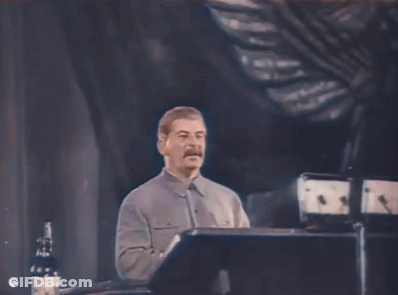 A Man With A Mustache Is Giving A Speech On A Stage GIF