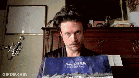A Man With A Mustache Is Holding A Book Called Pure Comedy GIF