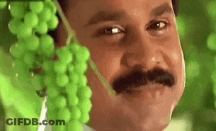 A Man With A Mustache Is Holding A Bunch Of Grapes Over His Face . GIF
