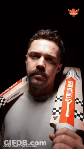 A Man With A Mustache Is Holding A Cricket Bat That Says Gray Nicolls GIF