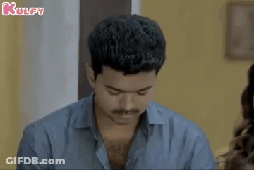 A Man With A Mustache Is Looking Down At Something While Sitting At A Table With A Woman . GIF