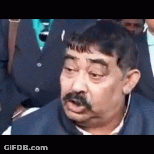 A Man With A Mustache Is Making A Funny Face While Sitting In Front Of A Group Of People . GIF