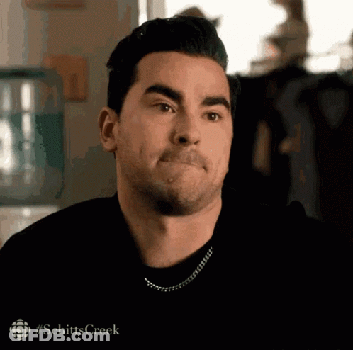 A Man With A Mustache Is Making A Funny Face While Wearing A Black Shirt And A Chain Around His Neck . GIF