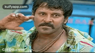 A Man With A Mustache Is Making A Funny Face While Wearing A Colorful Shirt . GIF