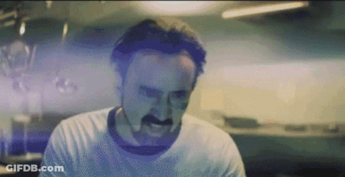 A Man With A Mustache Is Making A Funny Face While Wearing A White Shirt . GIF