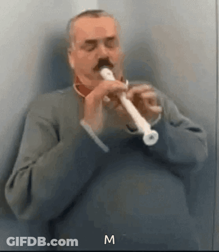 A Man With A Mustache Is Playing A Flute In A Room . GIF