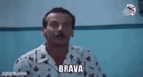 A Man With A Mustache Is Pointing At The Camera While Wearing A Shirt That Says Brava . GIF