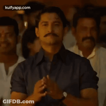 A Man With A Mustache Is Praying With His Hands Together In Front Of A Crowd Of People . GIF