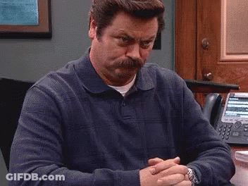 A Man With A Mustache Is Sitting At A Desk With His Hands Folded And A Watch On His Wrist . GIF