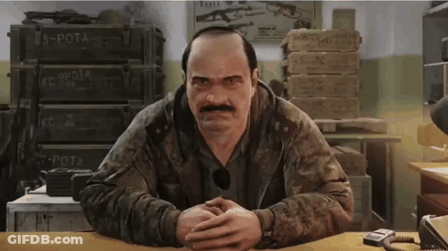 A Man With A Mustache Is Sitting At A Desk With His Hands Folded In Front Of A Stack Of Boxes . GIF