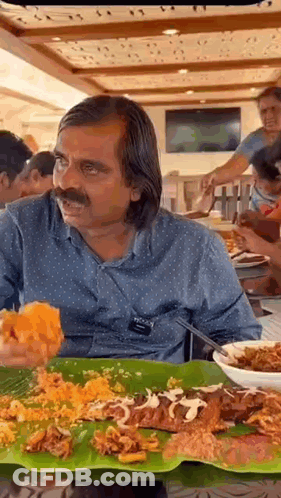 A Man With A Mustache Is Sitting At A Table Eating A Lot Of Food . GIF