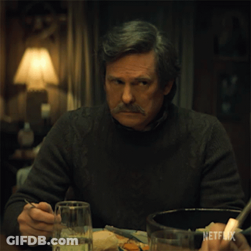 A Man With A Mustache Is Sitting At A Table With A Netflix Logo On The Bottom Right GIF