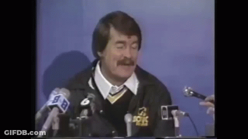 A Man With A Mustache Is Sitting At A Table With Microphones . GIF